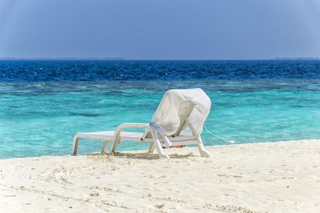 Eine weiße Liege am Strand vor türkisfarbenem Meer.